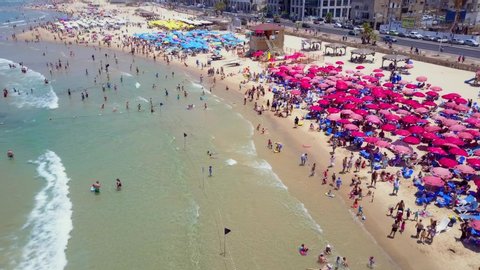 Tel Aviv, Israel - July 2, 2019: Aerial footage of People at Tel Aviv beach, with colourful umbrellas and clear Mediterranean Sea water.