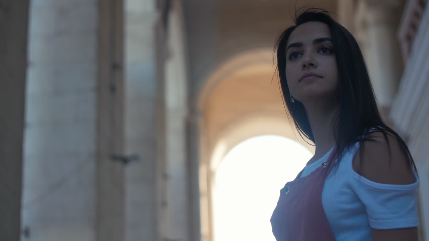 Portrait of young curious tourist girl standing near an old architecture building with arch, Slow motion