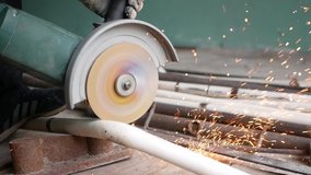 A man cuts metal pipes, slow motion video. sparks fly in all directions. Low light image of Worker ware yellow helmet kneel use electric steel cutter machine. He has a Hard work in Factory or garage