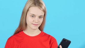 Close-up girl posing to the camera, holding a phone and speaking with someone using Video Calling on blue background. Slow motion