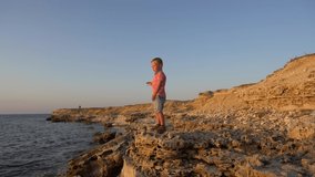 Child boy pick up a stone and throw it in a sea . Real emotions, boy on a sky background. Real positive emotions, real time video footage, boy on a blue sky background, 4K
