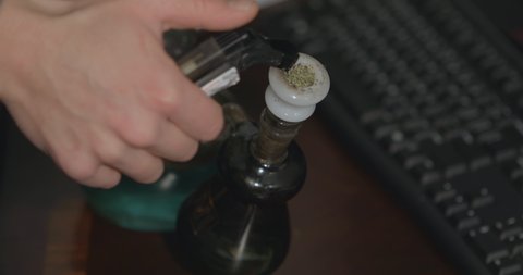 Smoke pours over a bong after a large hit of cannabis is taken on a wood office desk.