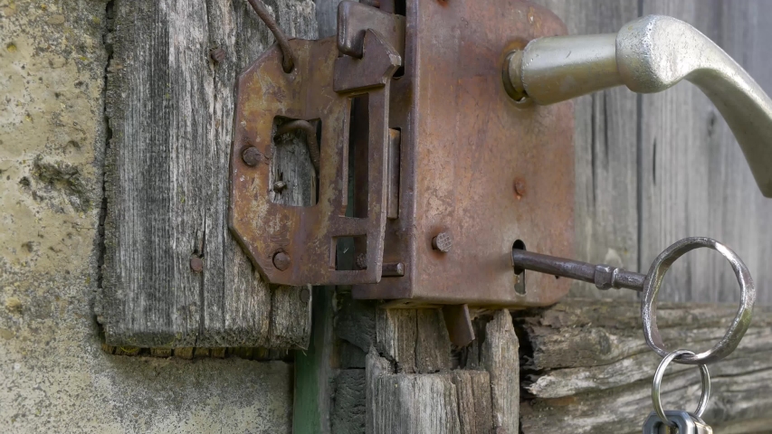 Caucasian man closing the rusty lock  on old wood door with a huge key. | Shutterstock HD Video #1035427076