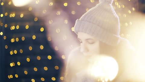 Girl check the Christmas present. Portrait sliding shot of young woman in focus wearing winter clothes and surrounded by decorative lights.