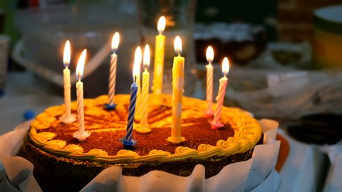 Beautiful delicious birthday cake with burning candles is on kitchen table. Maybe it was prepared for birthday celebration. Selective focus.
