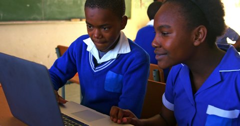 Front view close up of a young African schoolboy and schoolgirl sitting at a desk using a laptop computer together during a lesson in a township elementary school classroom, in the background