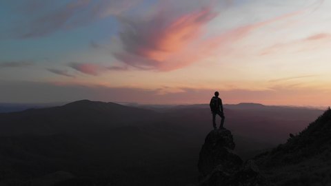 Person standing on rock with epic mountain viewpoint with a colorful sunset drone aerial landscape shot