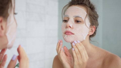 Close-up of a beautiful young woman applying a Korean sheet mask to moisturize the skin and smoothing it with her hands