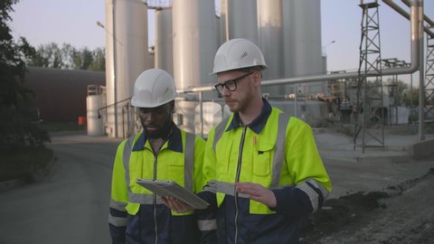 Two engineers discussing production of mining industry using digital tablet walking along industrial site