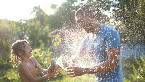 Father and son have fun in the garden, watering each other with water from a hose. Spray fly around, summer vacation, hot climate