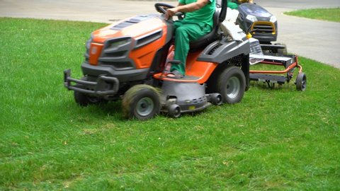 crop shot of workers riding on industrial lawn mowers and cutting grass in park