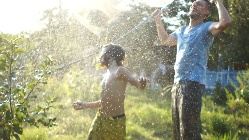 Father and son fooling around watering each other from a hose on a hot summer day. Holidays in the countryside, summer holidays Royalty-Free Stock Footage #1035441395