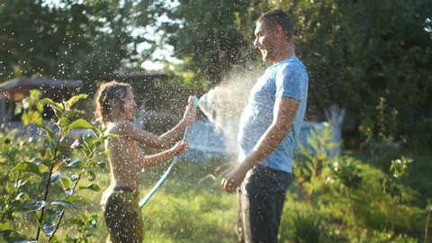 Curly-haired boy squirting his father with a hose. Holidays in the village, father's day