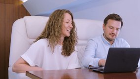 Making video conference call with colleague on laptop HUD hologram on board of private jet. Caucasian businessman and businesswoman travel inside of business airplane cabin.