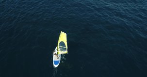 Aerial footage of windsurf woman alone in the blue sea. Windsurfing on the surface of the water.