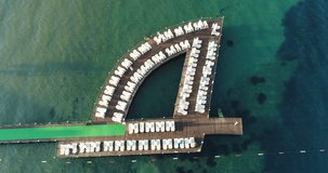 Aerial footage of wooden pier with ocean water, marina aerial view. Aerial drone view of touristic wooden pier in the middle of the blue sea with parasols and sunbeds on a summer day. Holiday Summer