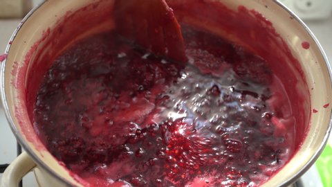 Cook raspberry jam and stir with a wooden spatula. Stir jam in a pan.