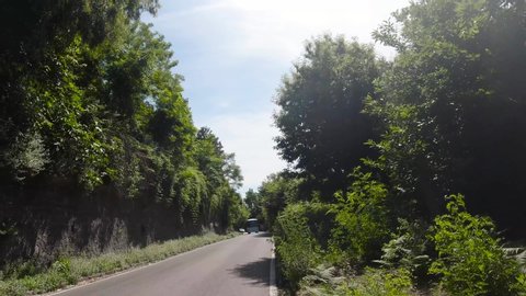 Naples, Italy, August 2019: POV dash camera tracking shot front view of driving in a curvy country road with trees in the side and a blue sky