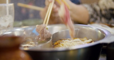 asian hand eating sukiyaki beef in hot pot .shabu shabu, close up shot