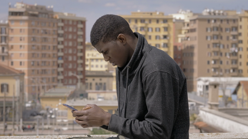 youg american african man typing on smartphone on building roof.Youth,technology