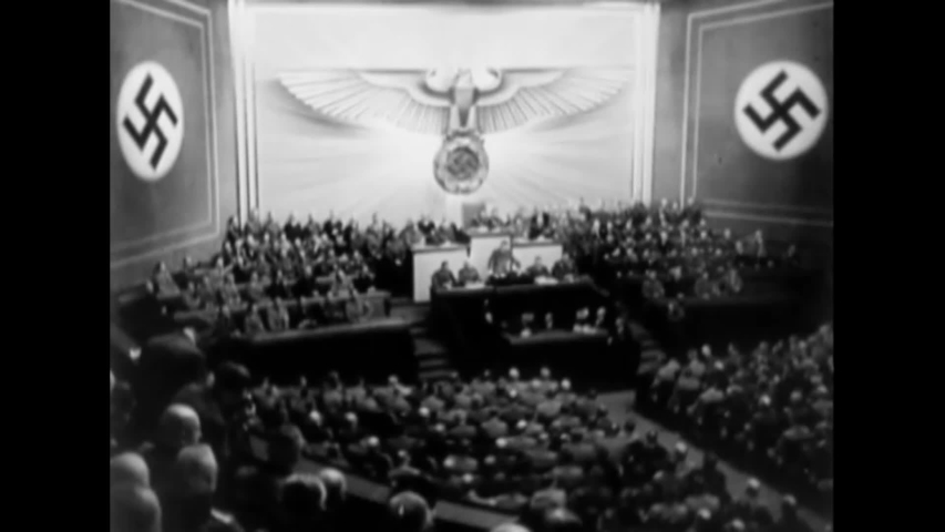 CIRCA 1939 - Hitler makes a speech in a German auditorium. German soldiers blow up buildings in Warsaw.