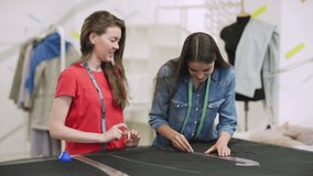 Tracking shot of professional tailor teaching young woman how to use sewing curve rulers to draw pattern on fabric with chalk during individual class - Powered by Shutterstock - Get 15% off with code: PIKWIZARD15