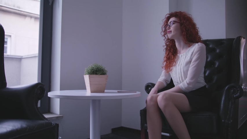 Woman is sitting in a  leather armchairs and talking on the phone 