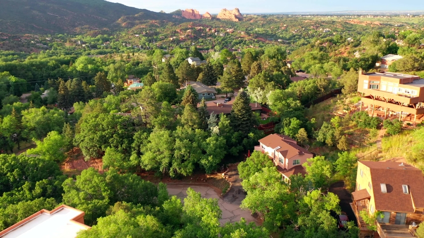 Aerial, drone shot, over buildings,towards the famous, red sandstone mountains, at the Garden of the Gods park, on a sunny evening, in Colorado springs, USA