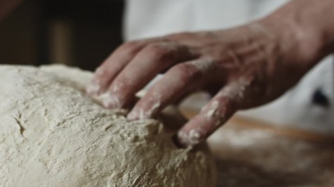  Close up view of baker kneading dough in flour on table.Manufacturing process, working hard. Making bread, bread production. Workplace. Beautiful view.
