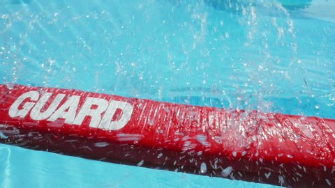 Red lifeguard float being thrown into a swimming pool. The bright rescue floatation device lands on the water, splashing drops onto the lens. Slow motion shot depicts search and rescue & saving lives.