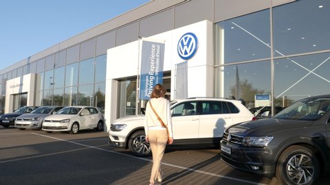 Strasbourg, France - Circa 2019: Rear view of young curious woman approaching admiring white Volkswagen Tiguan SUV car buy a new car at dealer shop