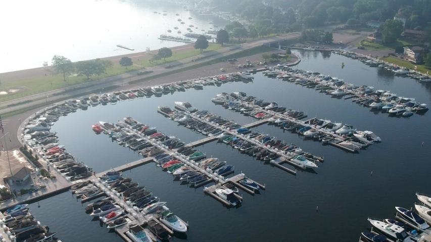 aerial drone footage of a pier full of various boats, yachts, and ships in lake Geneva in Wisconsin Illinois. its early morning sunrise as people begin to sail across the blue water with light fog