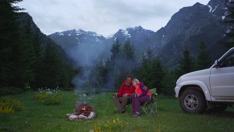 Couple chatting by bonfire in a camping in a dark mountain valley. White car