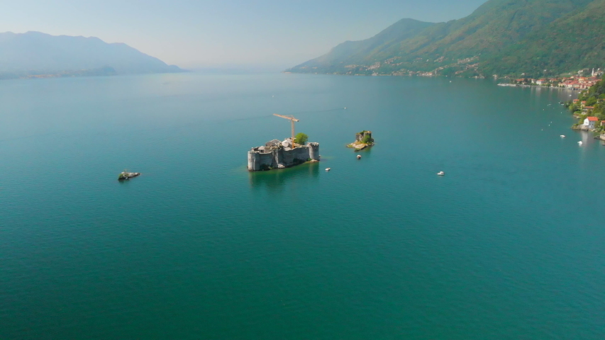 Aerial approach towards a small island with a ruin, sorrounded by tiny islands in the middle of Lake Maggiore, Italy