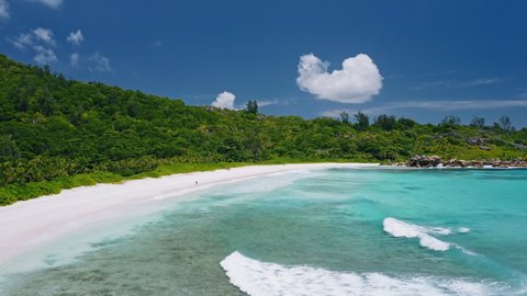 Aerial view of tropical paradise beach Anse Coco. Unrecognized lone tourist couple walk on white sand coast with blue blue lagoon and rolling waves. La Digue island, Seychelles