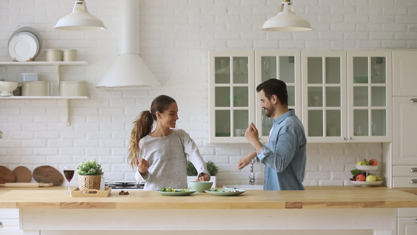 Young happy active family couple dancing laughing together preparing food at home, carefree joyful husband and wife having fun cooking healthy romantic dinner meal listen to music in modern kitchen | Shutterstock HD Video #1035500636
