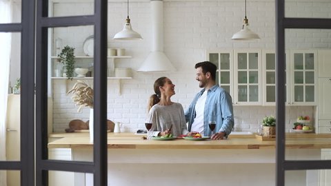 Happy loving young family couple cutting fresh vegetable salad having fun cooking together in modern cozy kitchen interior, smiling husband and wife bonding laughing helping prepare healthy meal