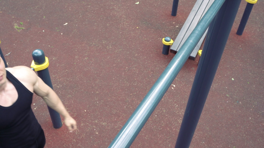Young athletic man doing push-ups on bars outdoors