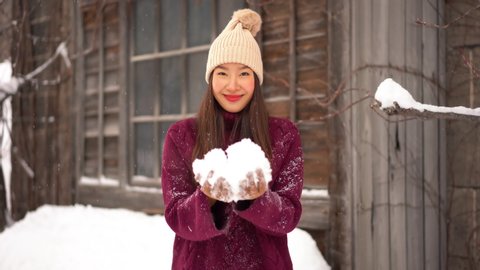 Happy Smiling Asian Female in Winter Clothes Holding Snow And Throw it In The Air