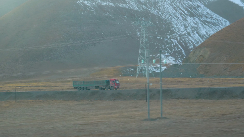 SLOW MOTION: View from a moving train of an old freight truck transporting goods across foggy Tibet. Cinematic shot of an 18 wheeler transporting cargo across scenic snowy plains in the Himalayas.