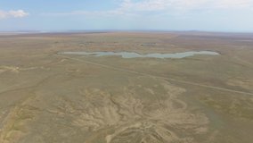Aerial: Steppe with dry plants and blue lake, uncultivated plains. Flight over steppe with dry plants and blue lake, uncultivated lands with country roads, aerial video