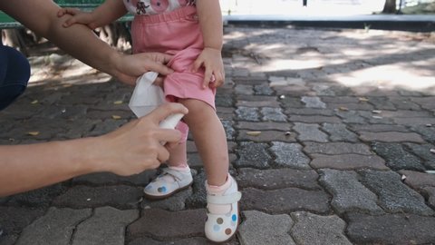 Scene of asian mother spray the mosquito repellent to 2 year old girl toddler on both legs before playing running in the park while kid jumping with excitement.
