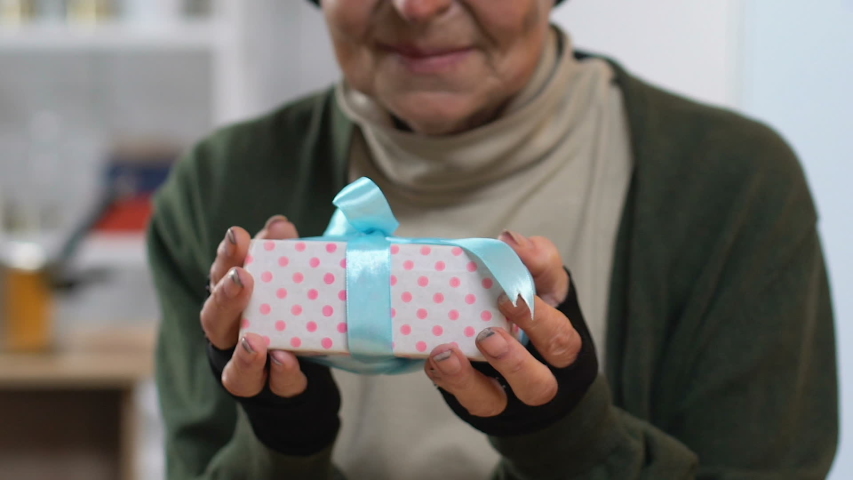 Smiling homeless woman holding gift box and looking to camera, pleasant surprise
