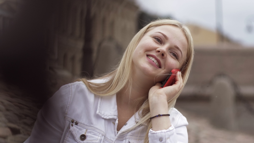 Close-up of beautiful positive young blonde girl sitting on the river embankment