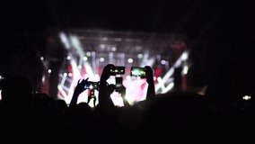 Abstract silhouette people in a crowd, hands up, dancing and holding smart phones. Out of focus stage. Handheld video
