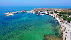 An aerial video footage of Paphos marina, Cyprus EU. Featuring a Mediterranean resort with turquoise bay, boats, promenade and a fort in a distance.