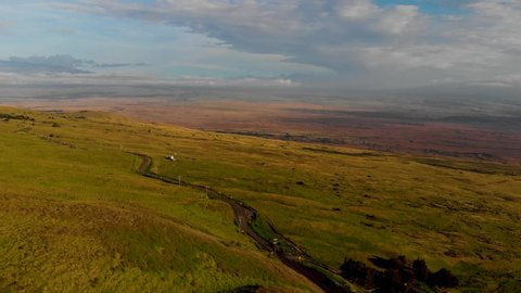 aerial drone view from Kohala mountain road, pan from left to right from Waimea to Kona in the distance. grassy fields on top of the slope are green and fade to golden brown in the distance.