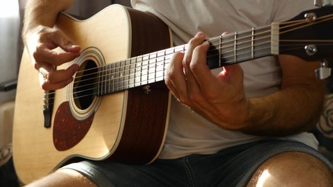 The musician plays a fast rhythm on a yellow acoustic guitar, a ray of light falls on the fingers and neck of the guitar