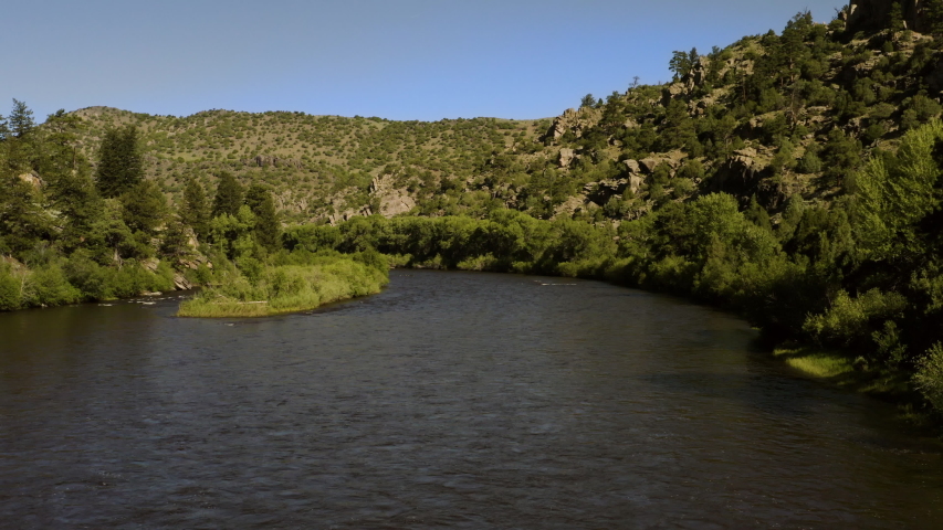 Aerial view along a wide river running through a valley of trees. Bennett Peak, North Platte River, Wyoming, USA | 4K
