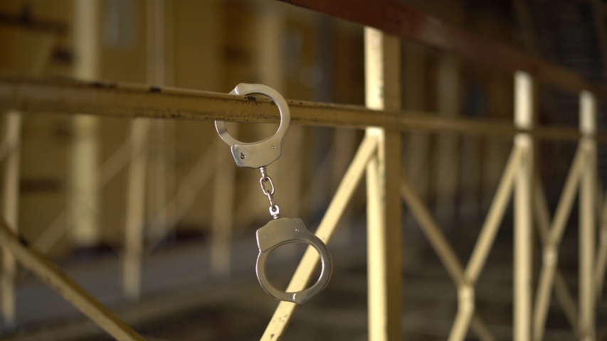 Handcuffs swinging on the handrail on a prison background. Concept: legal problems, criminal, offenses, waiting for the verdict of the judge,  white collar, convict, detainee, imprisonment, jail | Shutterstock HD Video #1035581180